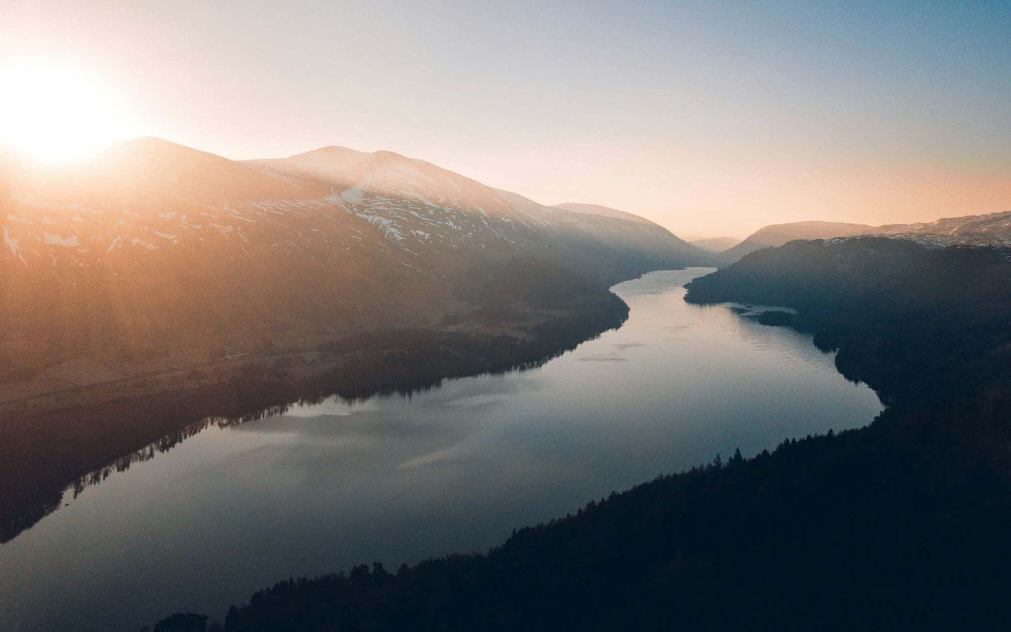 A lake winding through a valley between hills at dusk