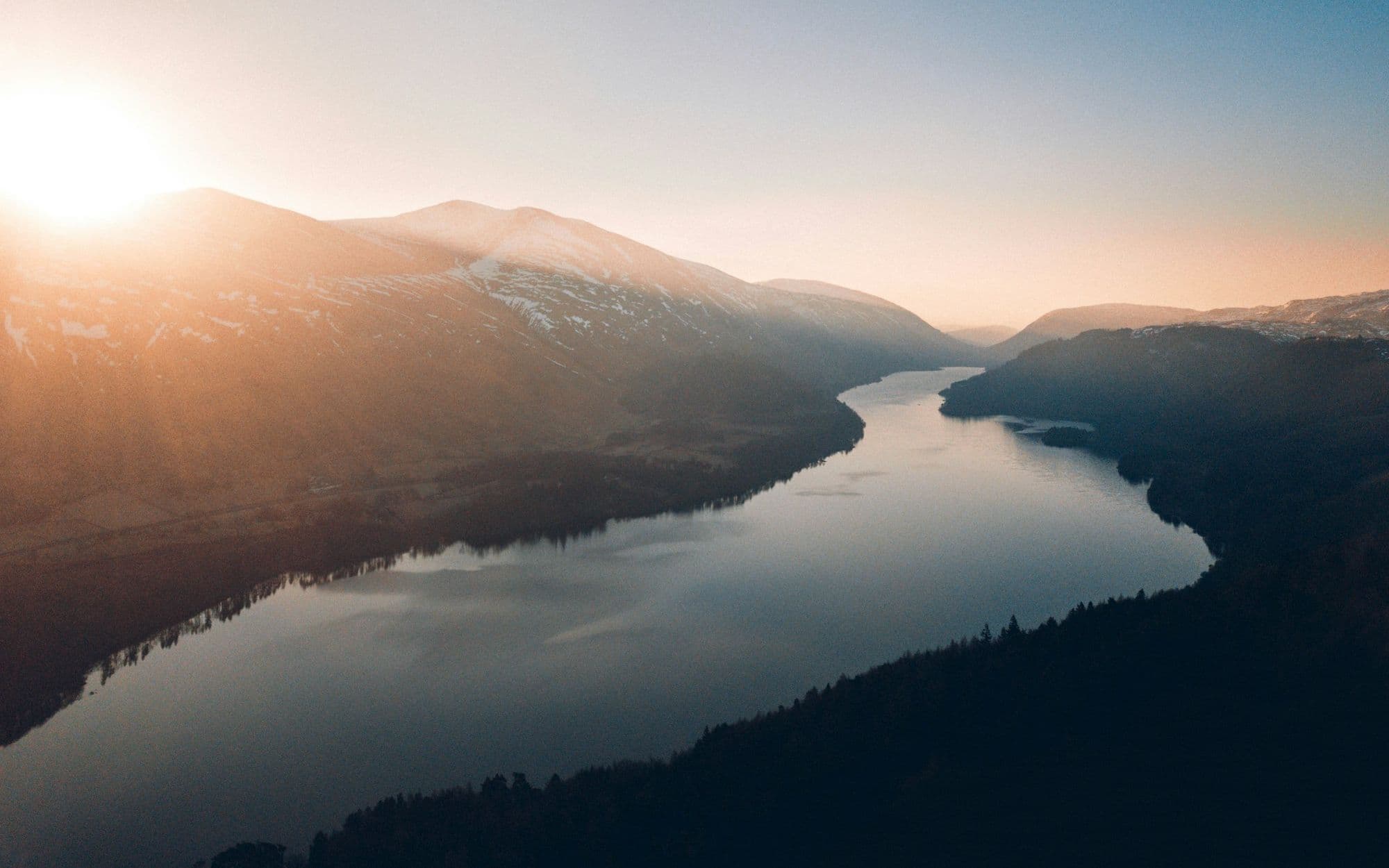 A lake winding through a valley between hills at dusk
