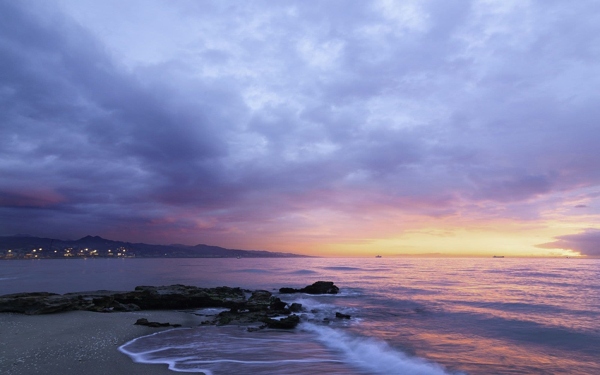 Slow waves rolling onto a shoreline under a lavender dusk sky