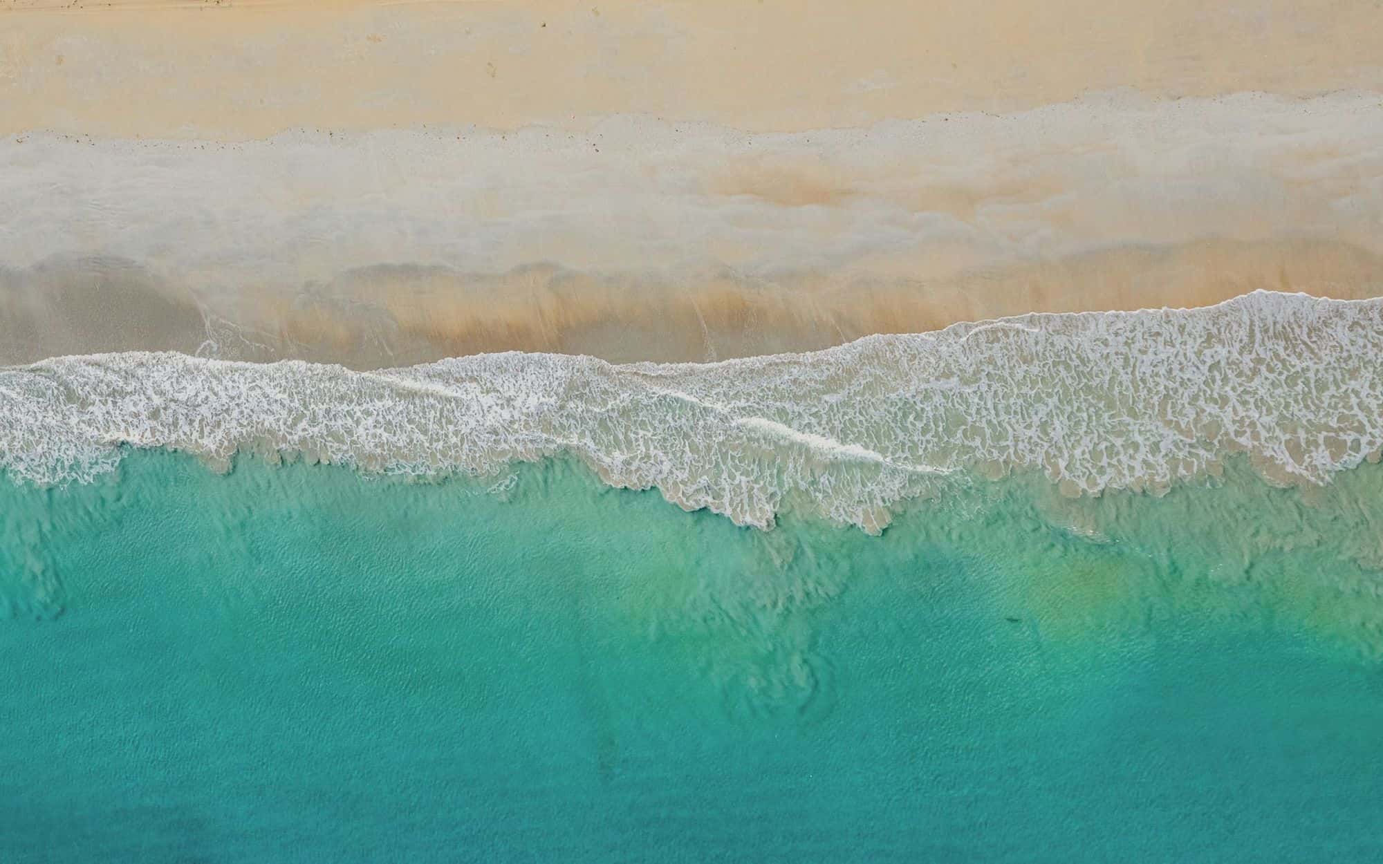 Turquoise waves meeting a sandy shoreline, seen from above