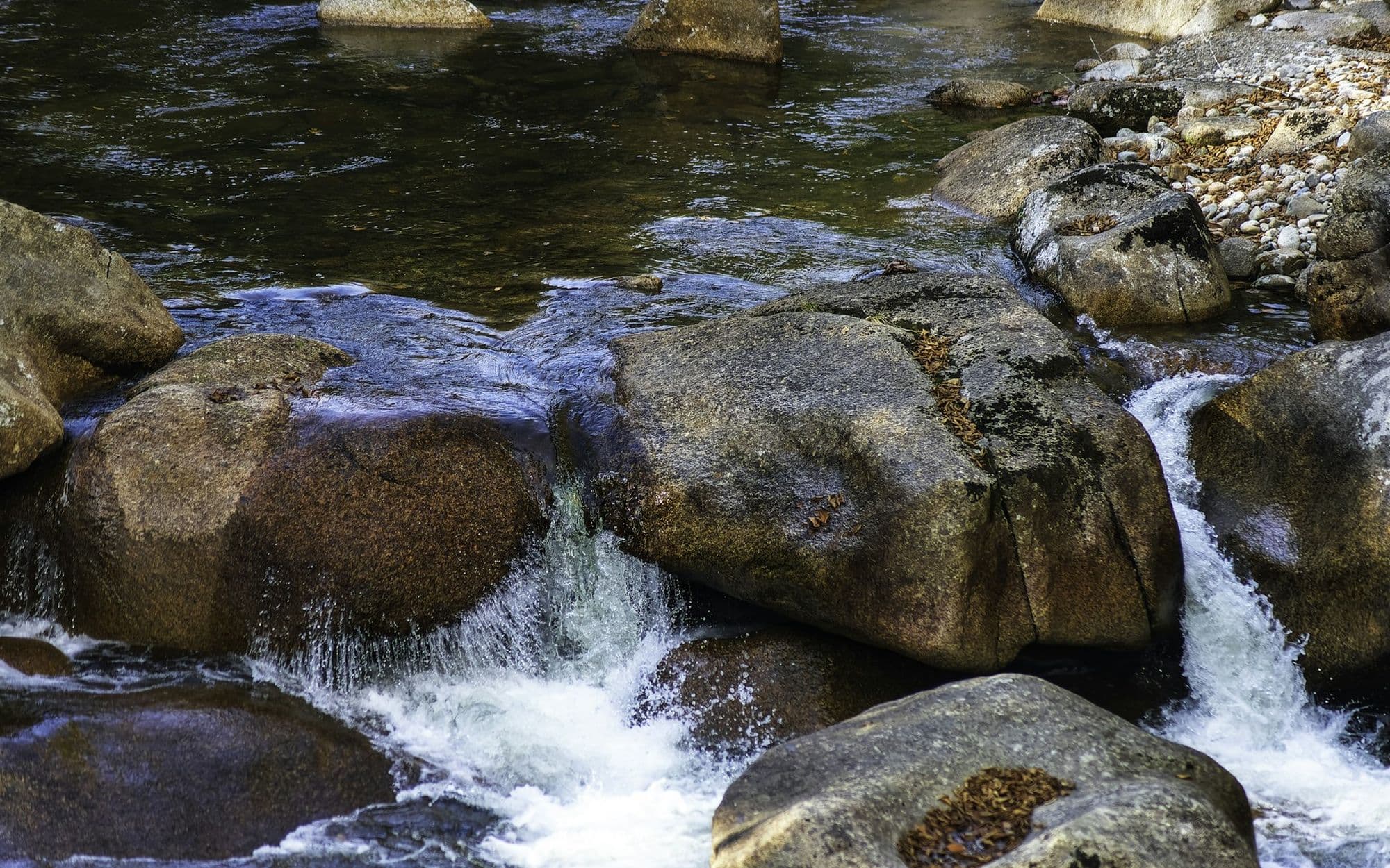 Clear water rushing over rounded granite stones