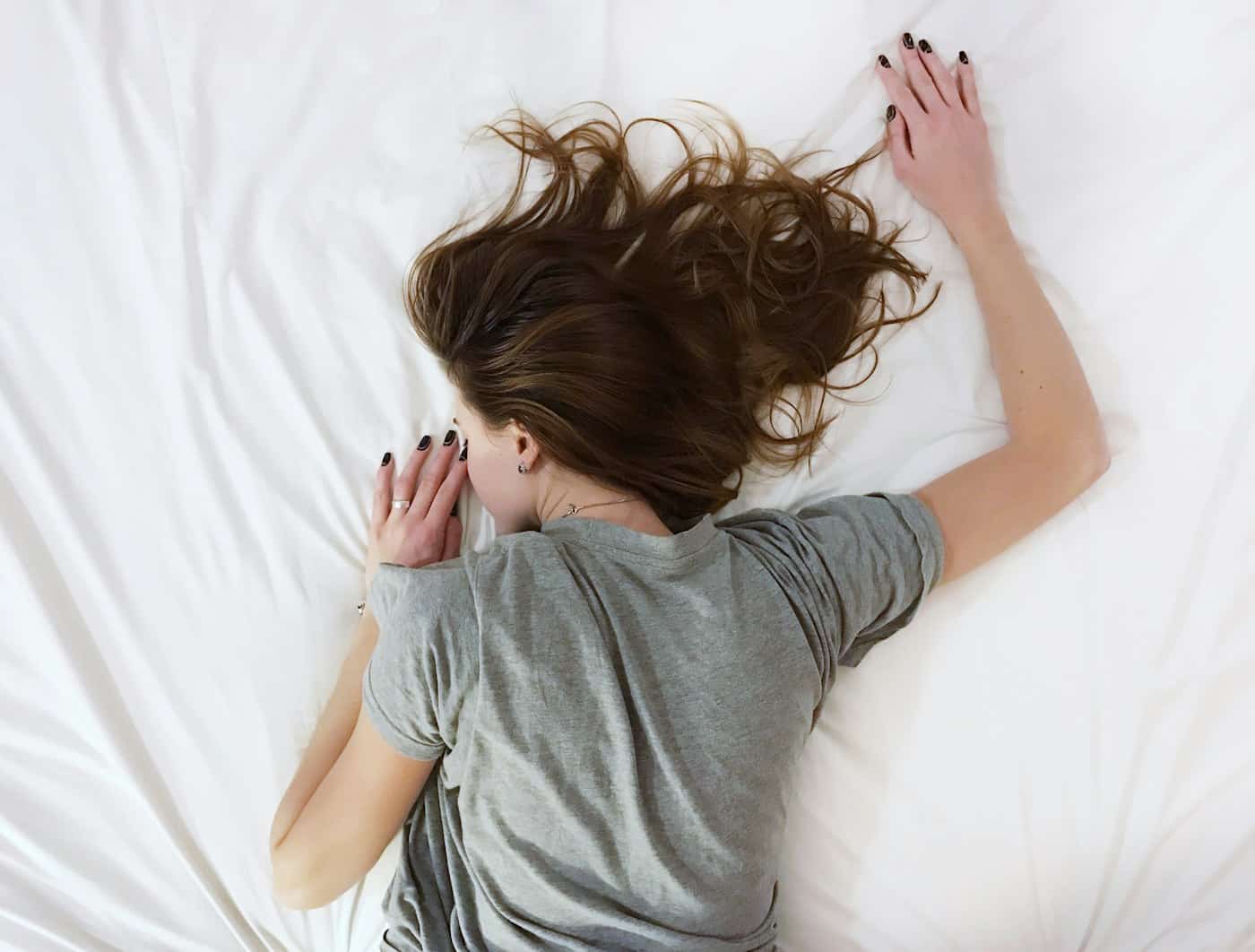 A person lying face down on pale bedding in early morning light