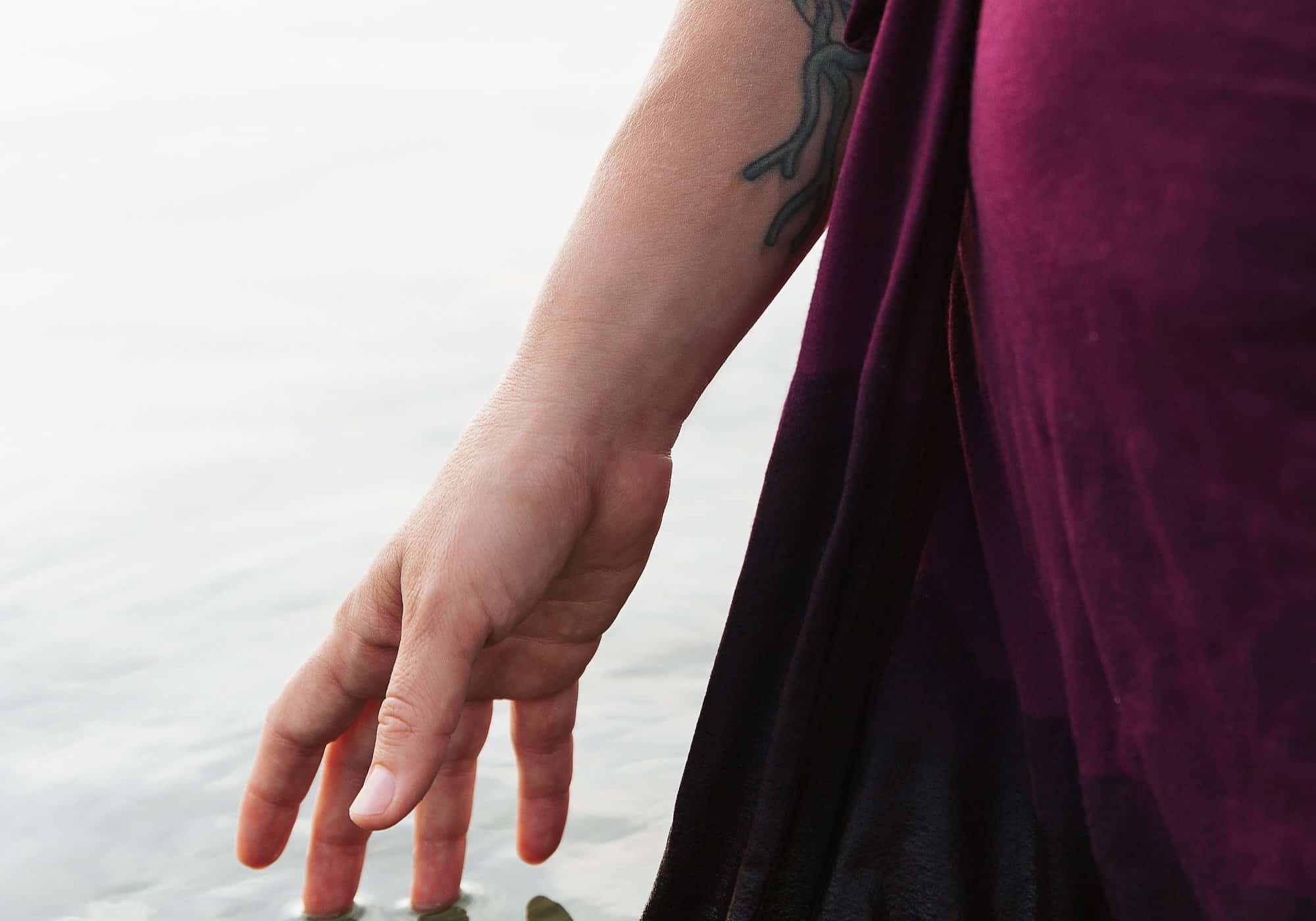 A hand trailing beside a flowing burgundy dress in soft light