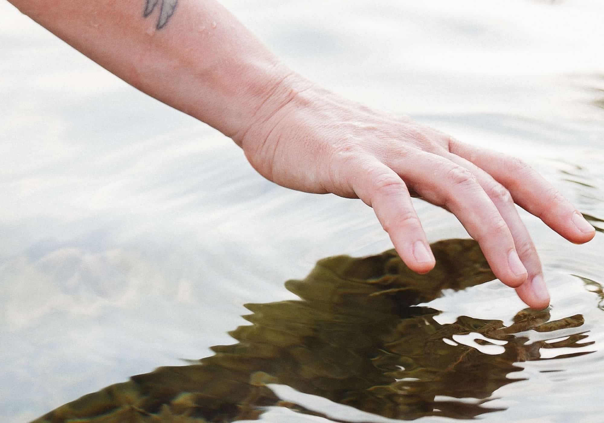 Fingertips resting on the surface of still, pale water
